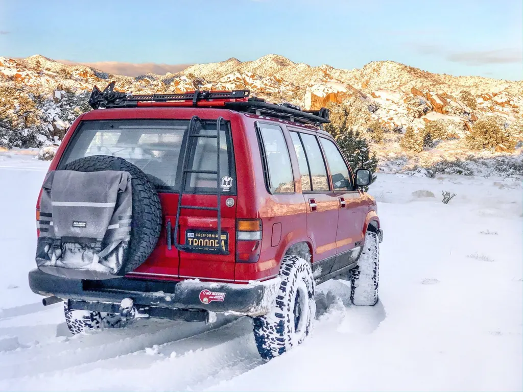 Red Isuzu Trooper in fresh snow below granite hills at sunrise