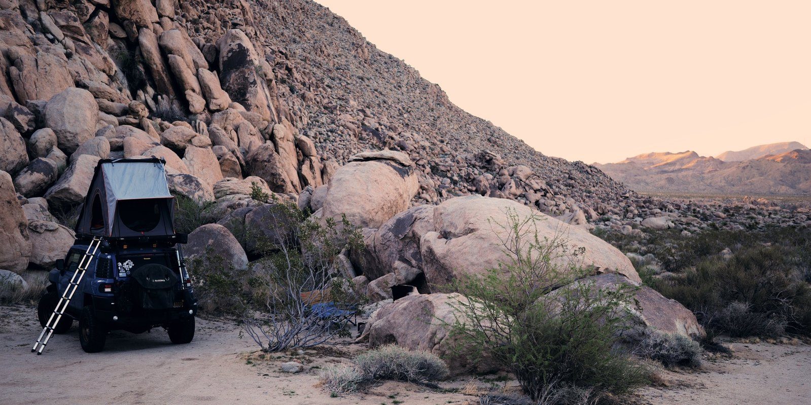 FJ with the tent open below a granite pile at dusk